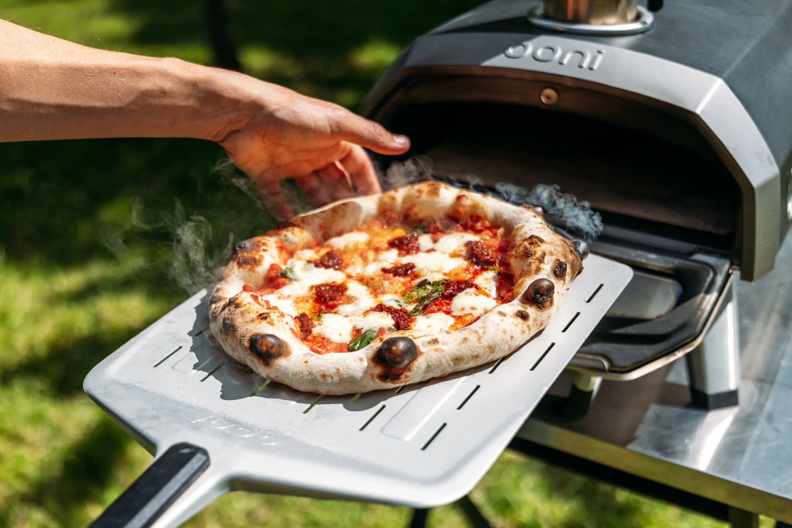 Fresh pizza being lifted from an outdoor Ooni oven