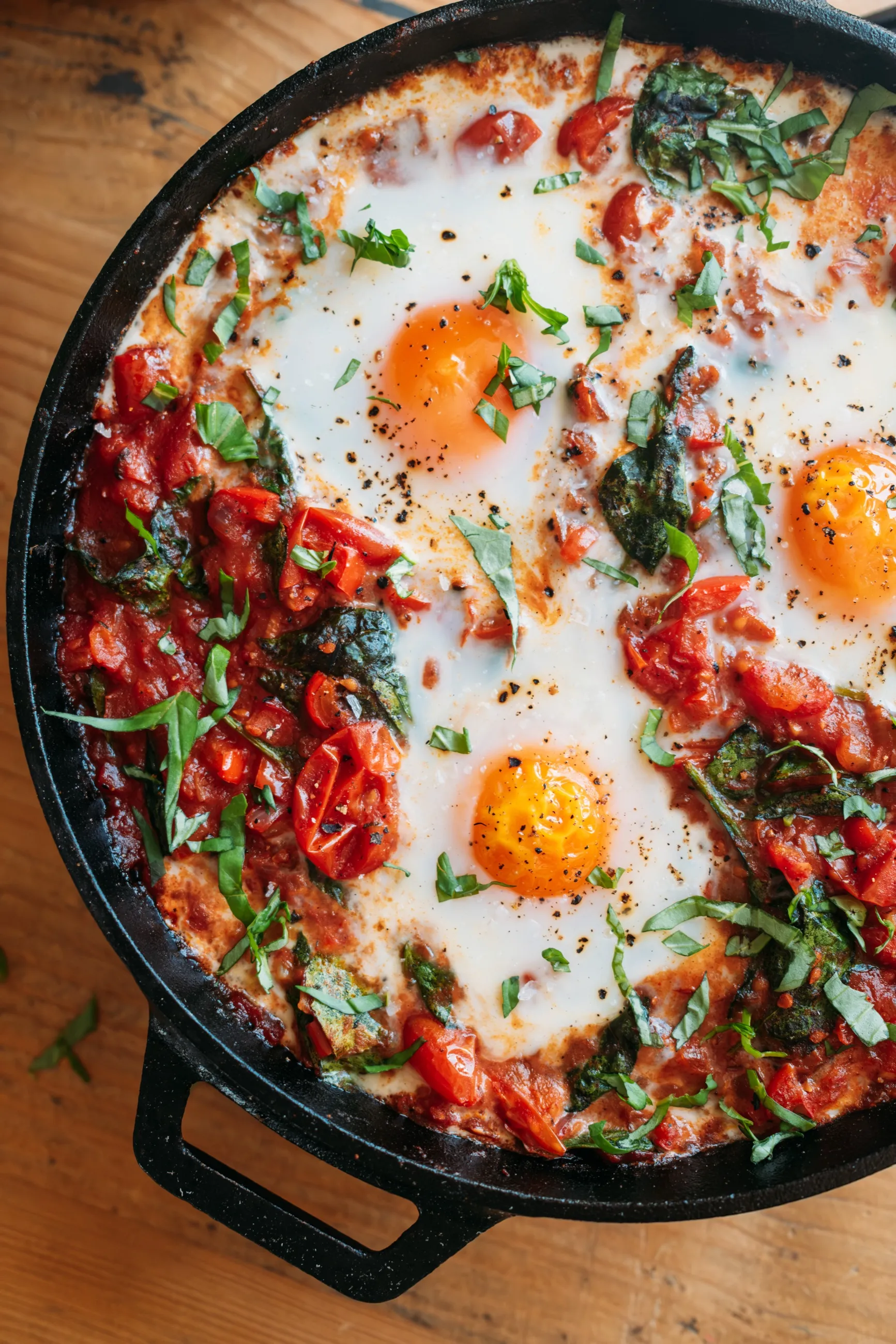 Baked eggs with tomatoes, greens and basil in a skillet